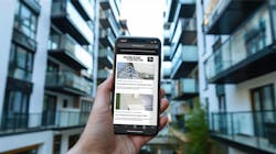 Hand holding smartphone in front of modern apartment building