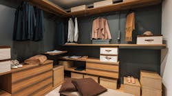Modern walk in closet showing organized clothes, shoes, and accessories. Interior of a modern and spacious walk in closet featuring wooden shelves, drawers, and organized clothing, shoes, and accessories