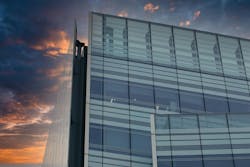 A modern glass and steel building against a colorful sunset sky. The building s facade features large windows and a grid pattern, while the sky is a blend of orange, purple, and blue A modern glass and steel building against a colorful sunset sky. The building s facade features large windows and a grid pattern, while the sky is a blend of orange, purple, and blue