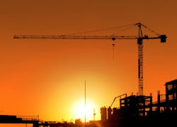 Construction Site and Crane. Horizontal photo of a construction site including a crane at sunset. The area is totally orange colored and all the buildings and equipment is seen as a silhouette