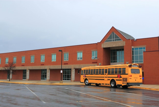 School Building with Bus. Red Brick School Building with Yellow School Bus at the front, ready for transporting students to home or drop off.