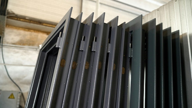 Stacked metal window frames with glass panes in workshop. Multiple dark gray metal window frames, complete with glass panes, are neatly stacked in a workshop environment